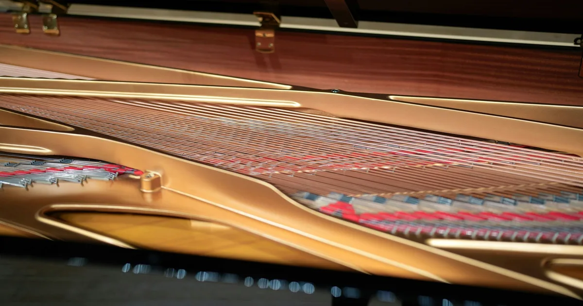 A close-up view inside a grand piano, showing the strings, tuning pins, and golden cast-iron frame.