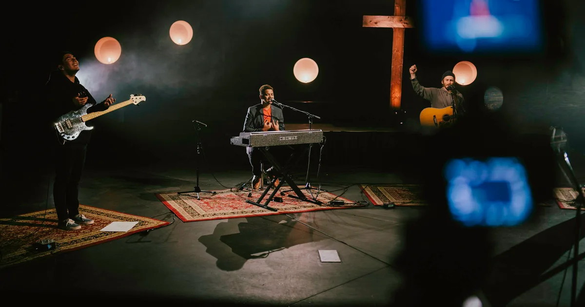 A pianist in dark clothing performing on a lit stage, hands at the keyboard.